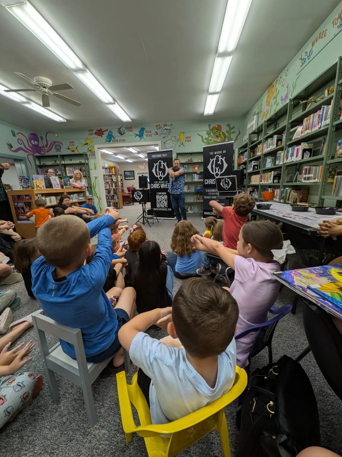 Children and families joining Chris Wheel in a library magic show